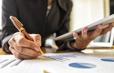 Woman holding tablet and pen reviews graphs on document