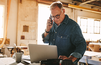 Businessman uses laptop while on cell phone call in warehouse