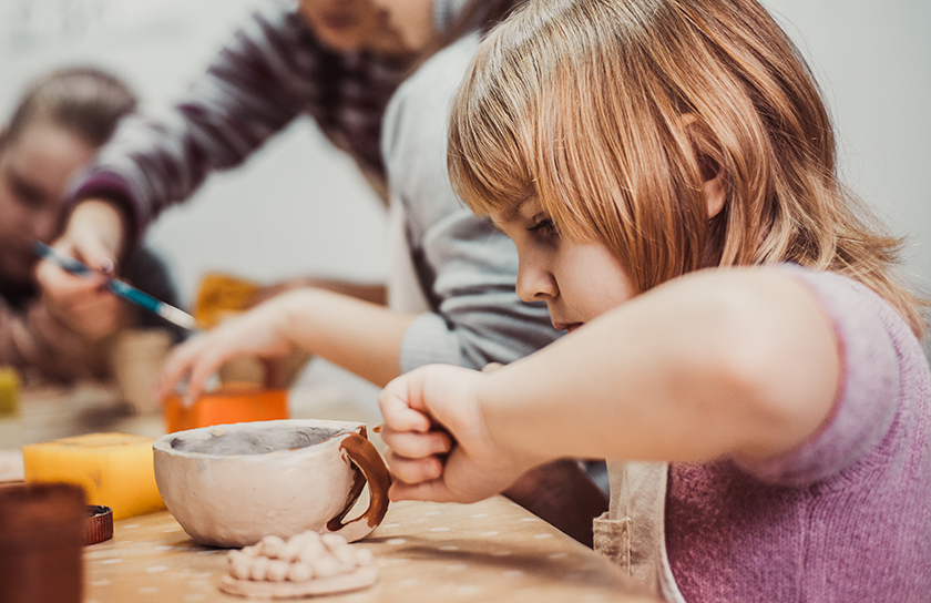 Child playing with arts and crafts at table with adults in background