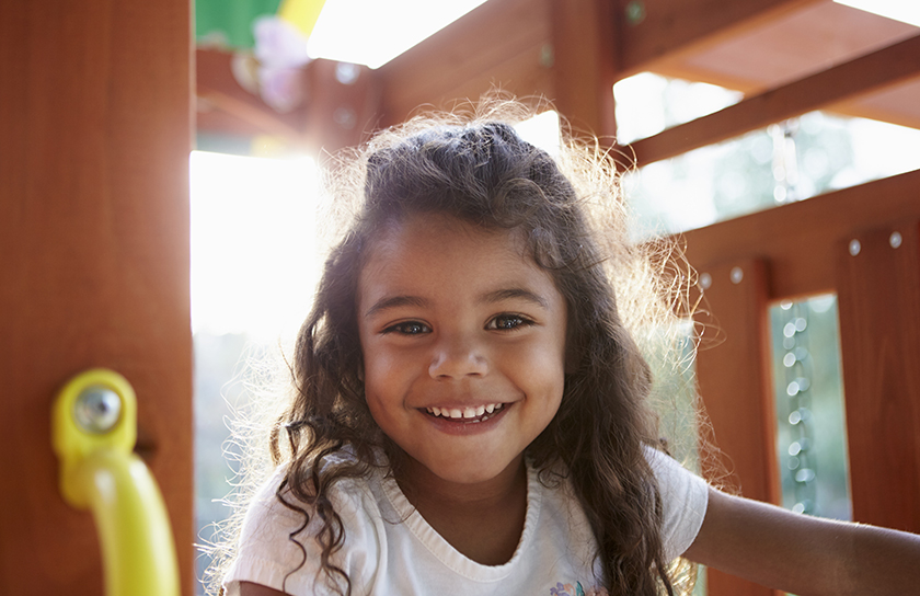 Little girl smiles while playing on child play set in park or backyard