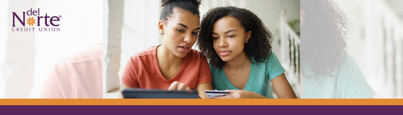 photo of two young friends looking at a phone and holding a credit or debit card