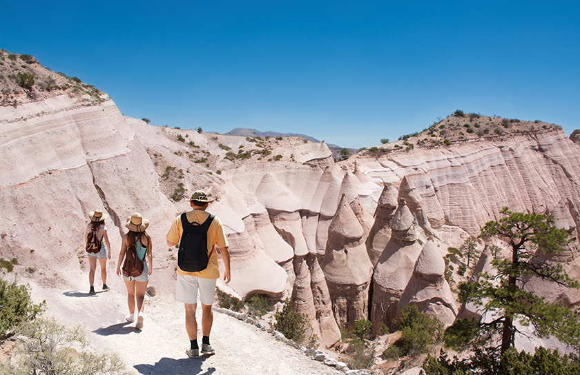 Three people with backpacks and wide brim hats walk in Tent Rock New Mexico