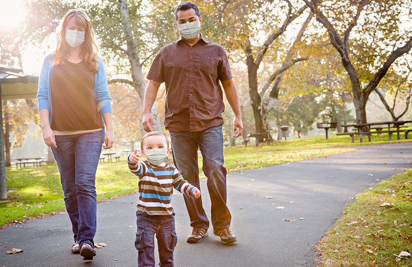 Two parents and toddler walk through public park with masks on their faces