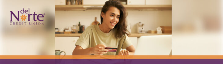 Woman sitting in kitchen looking at laptop holding credit card in hand