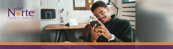 Smiling man sitting in home office looking at smartphone