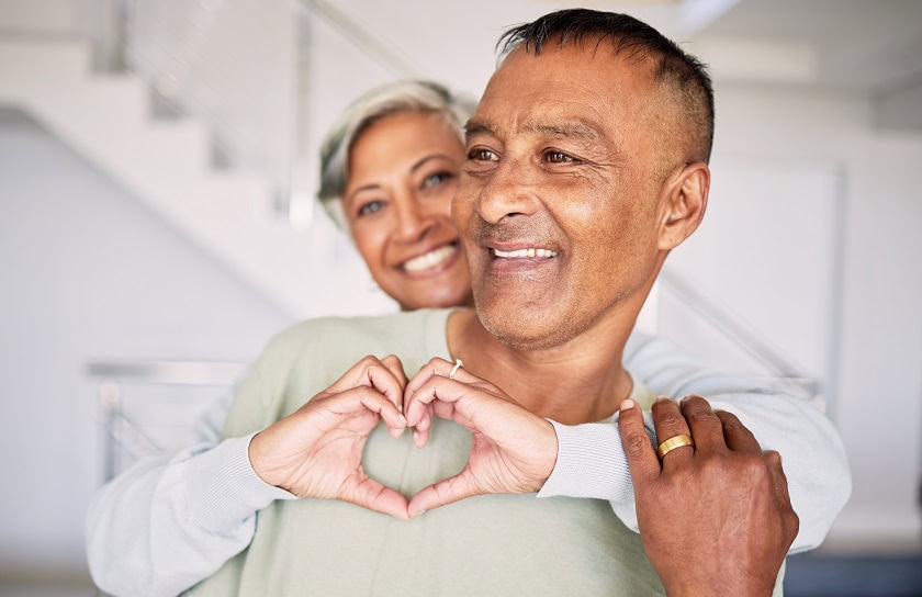 A woman hugs her spouse and forms a heart with her hands
