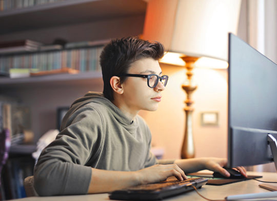 Boy with glasses sits in front of computer and keyboard in home office