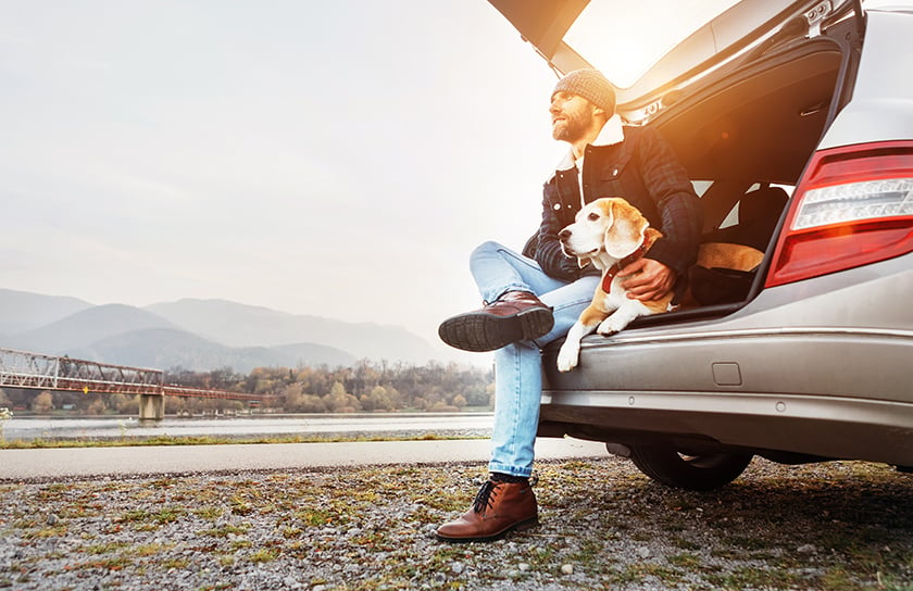 A man sits with his dog in trunk area of car near river