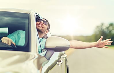 Man smiles and waves arm outside of vehicle while driving in New Mexico