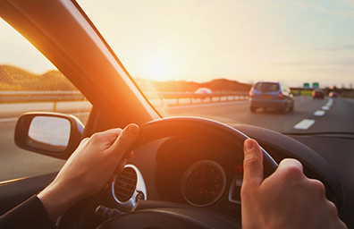 Car driver's hands on steering wheel while driving on highway at sunset