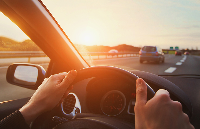 Pair of hands on steering wheel as car drives on highway