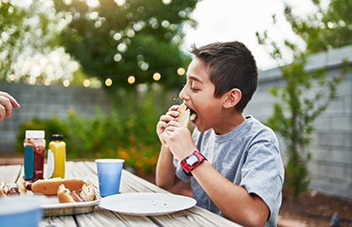 Young boy eats hot dog at backyard barbeque