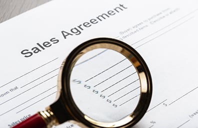 Magnifying glass pointed at sales agreement document