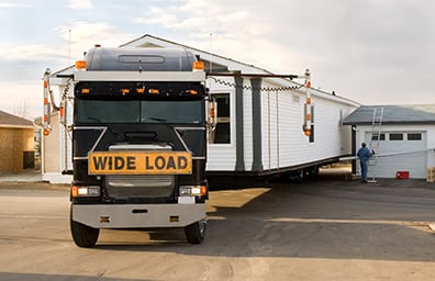 Truck carefully moves mobile home through narrow road