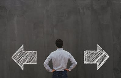 Man in suit looks at chalkboard with one arrow pointed left and another arrow pointed right