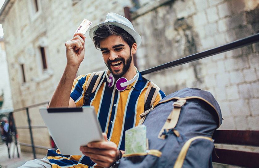 Happy Hispanic male traveler holds credit card in one hand and tablet in other hand