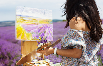 Woman paints lavender fields on art canvass while outside