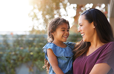 A woman holds her young daughter outdoors in afternoon sun