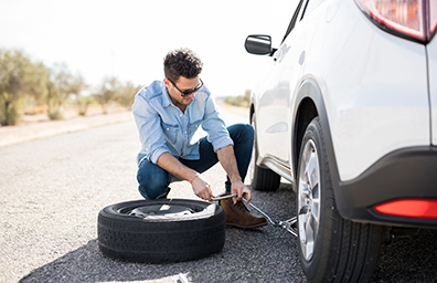 Young man fixes flat tire of car on side of desert road