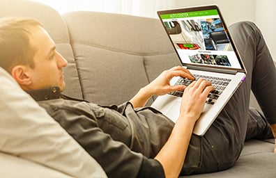 Man lying on couch shops for cars on laptop